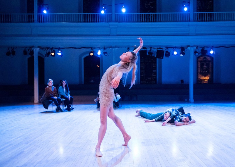 Sara Mearns looks up to the ceiling with her arm overhead; Rashaun Mitchell and Jodi Melnick lay in a heap in the background watching her